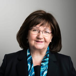 Angela Seeney smiling into the camera wearing a dark suit and blue scarf