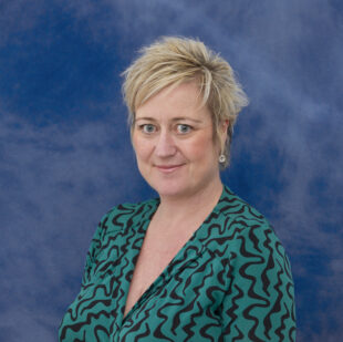 Hillary Crosthwaite with a blue background wearing a green patterned dress