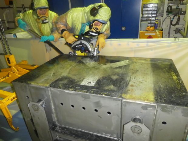 Two men in protective suits cutting up skip