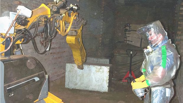 Sellafield worker in protective suit next to robot cutting up waste