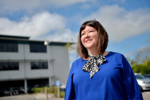 A woman in a blue top outside a building smiling