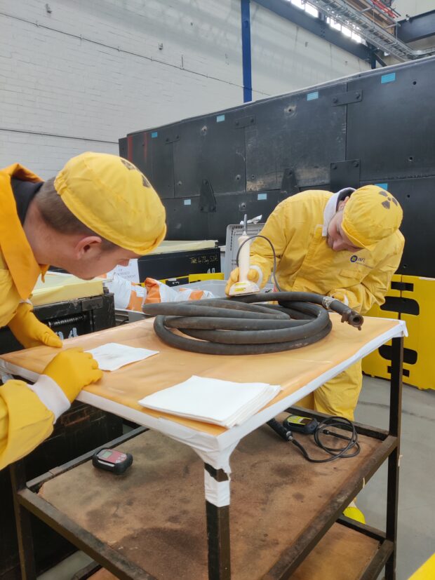 Joshua Bettles wearing PPE carries out a monitoring task under the supervision of a worker from Sizewell A