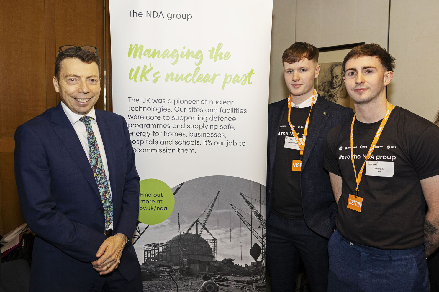 Two apprentices and Chair of the NIA stood beside a corporate NDA pop-up banner